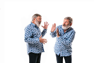 Senior man arguing with himself on white studio background. Concept of human emotions, expression, mental issues, internal conflict, split personality. Half-length portrait. Negative space. Scared.