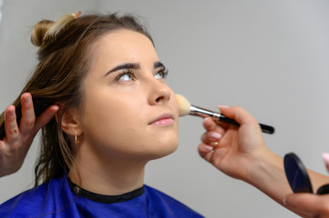 Fototapeta premium Studio photo of the work of a makeup artist by a hairdresser beautician. Creating beautiful makeup and hairstyles, rejuvenating the skin of the face. The professional is working with special tools.