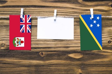 Hanging flags of Bermuda and Solomon Islands attached to rope with clothes pins with copy space on...