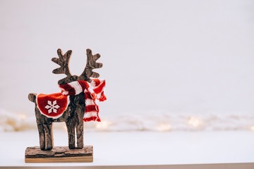 Wooden and furry deer statuette on a white background of snow and lights