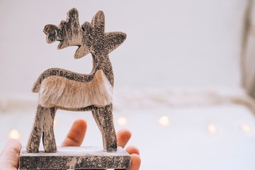 Wooden christmas deer statuette with red scarf on a hand with white background of snow and lights