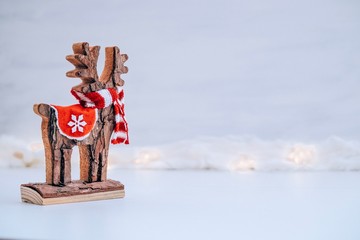 Wooden christmas deer statuette with red scarf on a white background of snow and lights