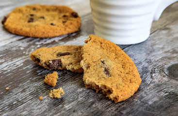 Freshly prepared chocolate chip cookies, partially eaten seen on a wooden kitchen surface together with a coffee mug.