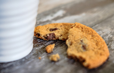 Freshly prepared chocolate chip cookies, partially eaten seen on a wooden kitchen surface together with a coffee mug.