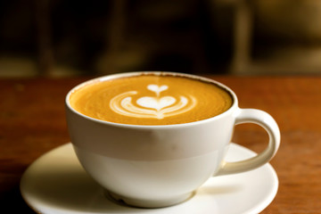 White cup of cappuccino with latte art on wooden background at coffee cafe.