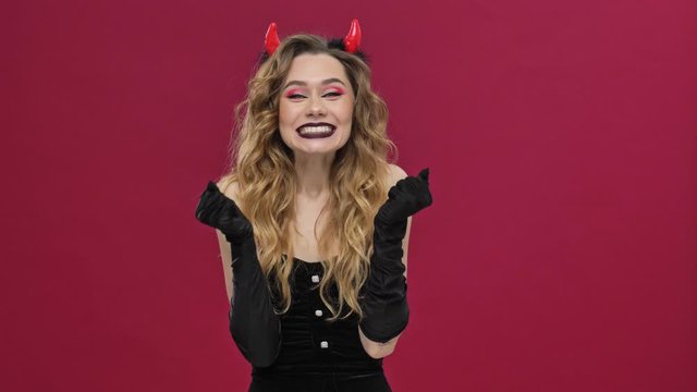 Happy positive devil woman in carnival costume is showing a winner gesture isolated over red wall background 