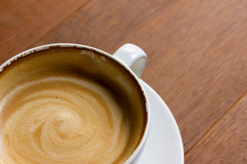 White cup of cappuccino with latte art on wooden background at coffee cafe.