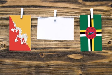 Hanging flags of Bhutan and Dominica attached to rope with clothes pins with copy space on white note paper on wooden background.Diplomatic relations between countries.