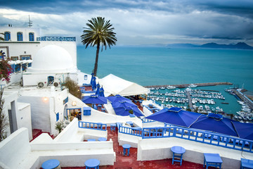 Terrace Balconies of Historic Sidi Bou Said, Harbor, and Mediterranean Sea under a stormy sky -...