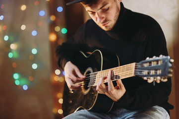 Obraz na płótnie Canvas handsome romantic guy plays the guitar. background of lights