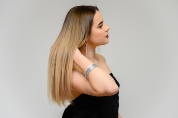 Naklejka premium Studio portrait of a beautiful girl with long beautiful hair and excellent make-up on a gray background in different poses. She smiles.