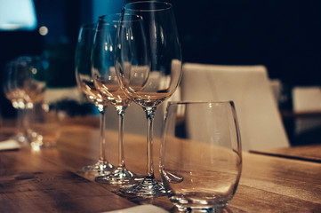 Empty glasses on wooden table, served for wine tasting event. Bar or shop interior, subdued light, lovely atmosphere. Selective focus. Film Grain effect. Low Key Image