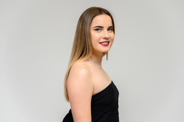Naklejka premium Studio portrait of a beautiful girl with long beautiful hair and excellent make-up on a gray background in different poses. She smiles.