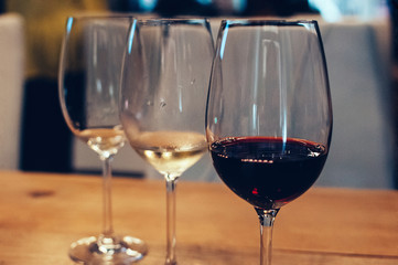 three glasses with red and white wine, on wooden table, served for wine tasting event. Blurred background. Bar or restaurant interior, subdued light. Selective focus. Flm Grain effect