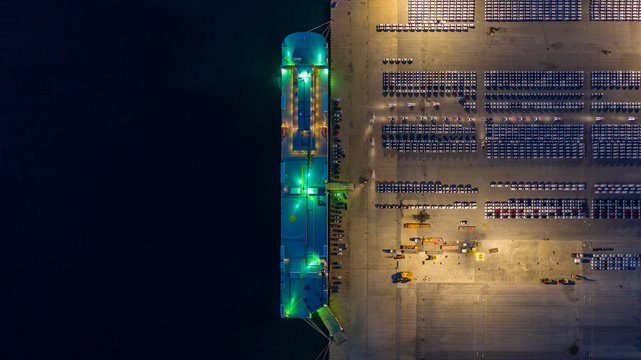 Aerial view rows of new cars at night waiting to be dispatch and shipped, New cars lined up in the port for import export around the world,  Car carrier vessel.