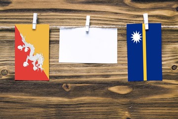 Hanging flags of Bhutan and Nauru attached to rope with clothes pins with copy space on white note paper on wooden background.Diplomatic relations between countries.