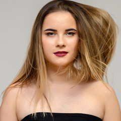 Naklejka premium Studio large photo portrait of a beautiful girl with long beautiful flowing hair and excellent make-up on a gray background in different poses. She smiles.
