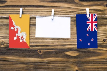 Hanging flags of Bhutan and New Zealand attached to rope with clothes pins with copy space on white note paper on wooden background.Diplomatic relations between countries.