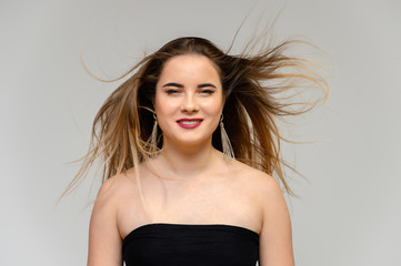 Studio large photo portrait of a beautiful girl with long beautiful flowing hair and excellent make-up on a gray background in different poses. She smiles.