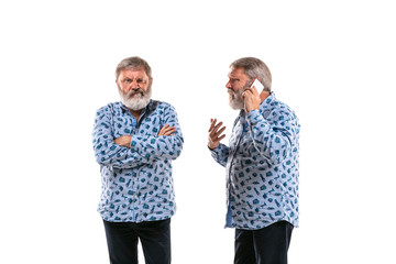 Senior man arguing with himself on white studio background. Concept of human emotions, expression, mental issues, internal conflict, split personality. Half-length portrait. Negative space. Gremaces.