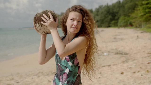 Puzzled female shaking coconut on beach