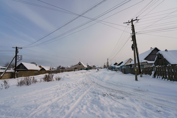 Fototapeta na wymiar Cold snow white Russian winter. Traditional village in sunny sunset. The concepts of beauty of nature, rural lifestyles and ecological tourism. Back lit