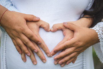 Manos haciendo la forma de corazón en la barriga de una mujer embarazada