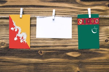 Hanging flags of Bhutan and Turkmenistan attached to rope with clothes pins with copy space on...