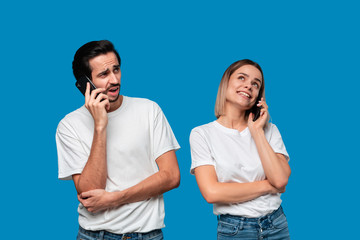 Blond woman and brunet man in white tees and blue jeans are talking on the phone.