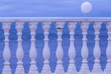 Promenade overlooking the sea through the fence on a gloomy rainy day. White balloon in the wind tied to the fence. Beautiful seascape.