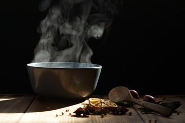 Hot soup with steaming and smoke in black bowl on wooden table with dark background. hot food...