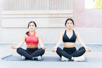 Female Athletes Sitting In Lotus Position On Footpath