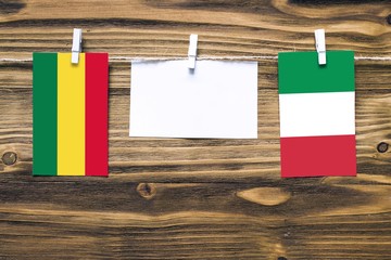 Hanging flags of Bolivia and Italy attached to rope with clothes pins with copy space on white note paper on wooden background.Diplomatic relations between countries.