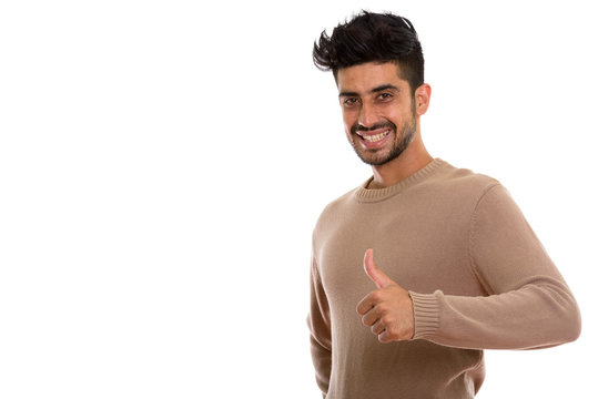 Studio shot of young happy Persian man smiling while giving thum