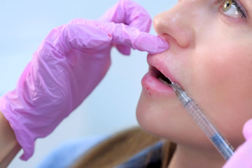 Naklejka premium Injection in patient woman lips to volume and correction shape making by doctor cosmetologist. Beautician injects filler collagen or hyaluronic acid into lips with syringe. Contour Plastic of Lips.