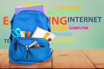 Open blue school backpack on wooden desk and gradient background.