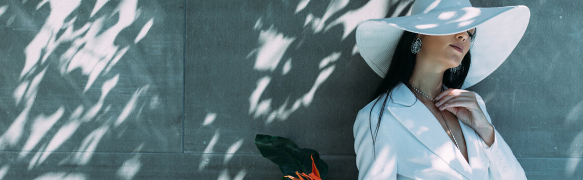 panoramic shot of attractive woman in white suit and hat posing outside