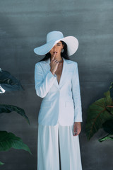 attractive woman in white suit and hat posing and obscuring face outside