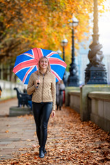 Junge, blonde Frau läuft durch das herbstliche London, Großbritannien, mit einem Regenschirm mit Britischer Fahne