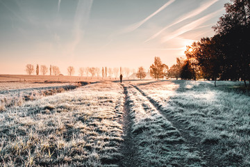 Relax nature walking in an winter morning landscape with frozen grass and colorful sunrise light and a girl enjoying the landscape view