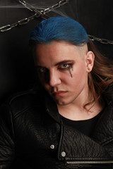 Teen alt boy with blue hair and shaved head dressed in black on dark background