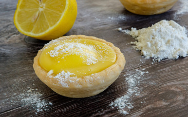 Close-up view of a freshly made lemon cake shown on a traditional work surface together with baking flour on the icing and heaped on the work surface, together with a slice lemon in the background.