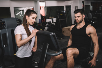 attractive trainer instructing handsome sportsman working out on recumbent elliptical trainer