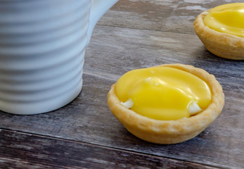 Pair of freshly baked lemon cakes shown on a traditional wooden table together with a partial view of a large, ceramic coffee much on the work surface