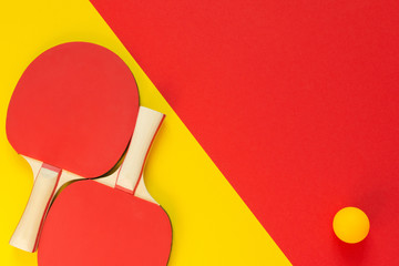 Red tennis ping pong rackets and orange ball isolated on a red and yellow background, sport...