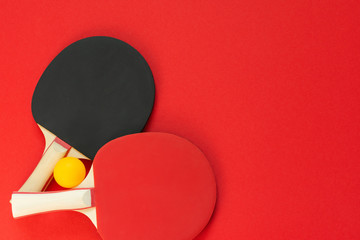Black and red tennis ping pong rackets and orange ball isolated on a red background, sport...