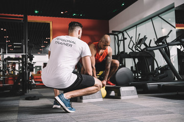 Back view of personal trainer supervising African American athlete lifting weight in gym