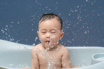 Cute baby boy bathes in a bathtub play and making splash water drops, smiling cheerful. Concepts for health care and daily routine.