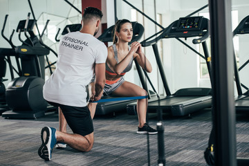 back view of personal trainer supervising young sportswoman exercising with resistance band