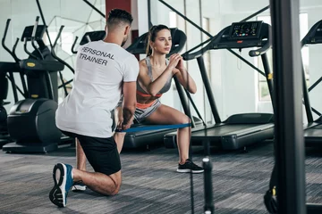 Fotobehang back view of personal trainer supervising young sportswoman exercising with resistance band © LIGHTFIELD STUDIOS